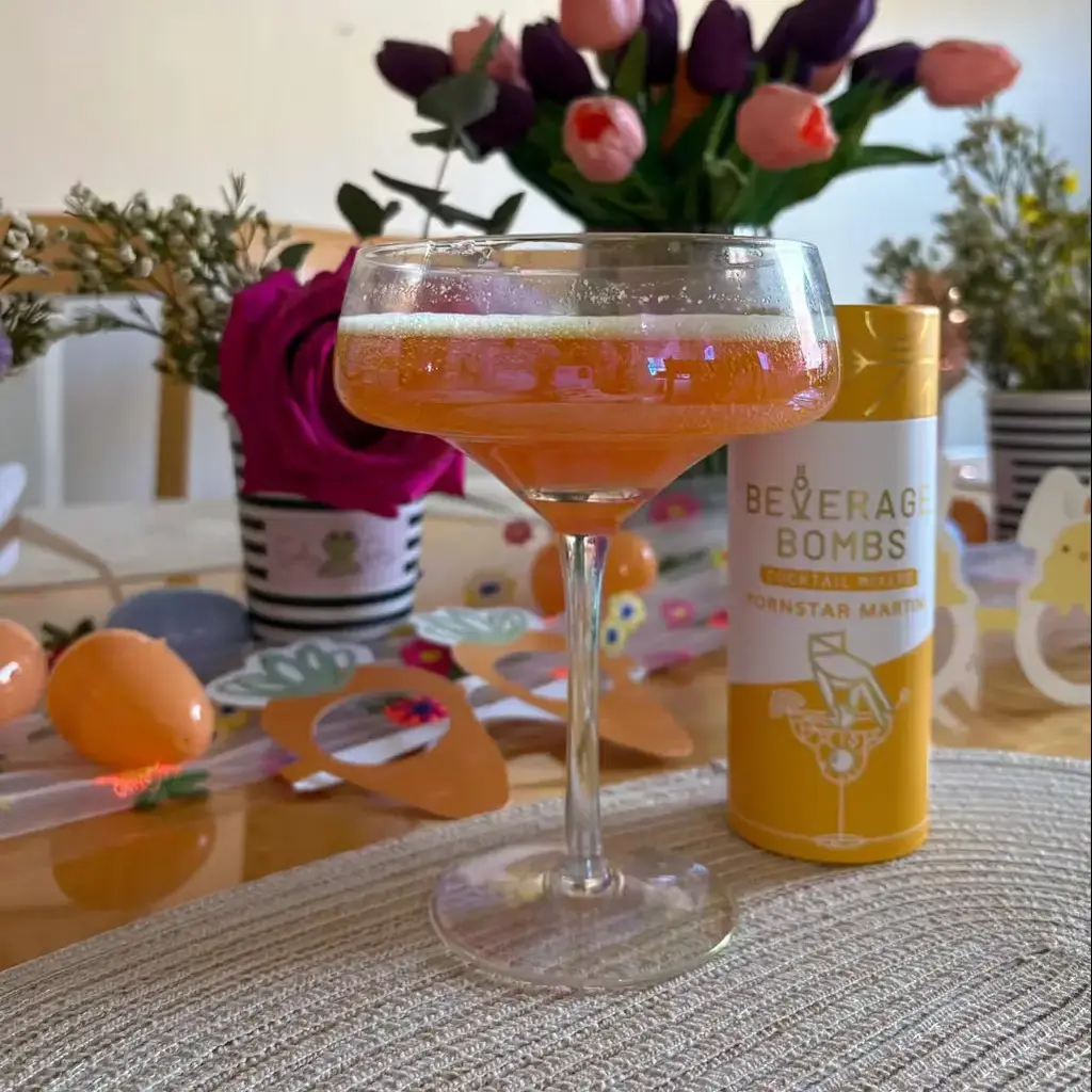 A cocktail glass with orange drink, surrounded by flowers and a beverage can.