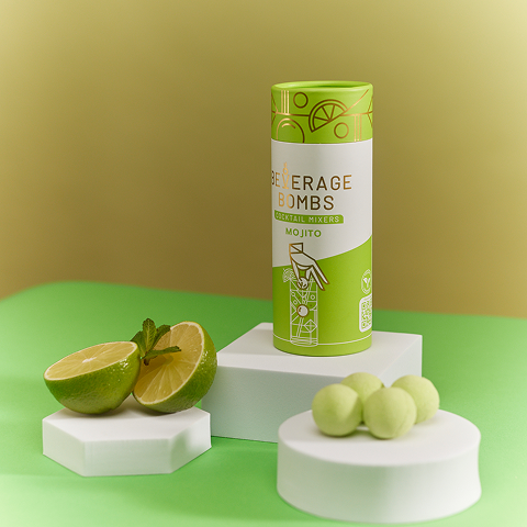 A tube of Mojito Beverage Bombs cocktail mixers next to a cut lime, mint, and several bombs.