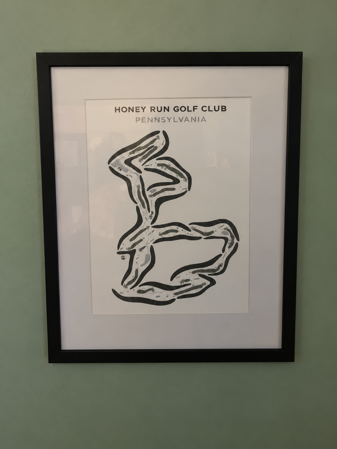A framed print of the Honey Run Golf Club course layout in Pennsylvania hanging on a green wall.