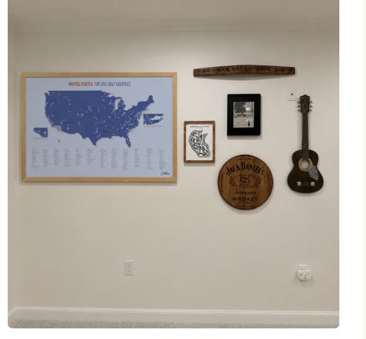 A wall decorated with a large framed map of US golf courses, a guitar, and other assorted wall art.