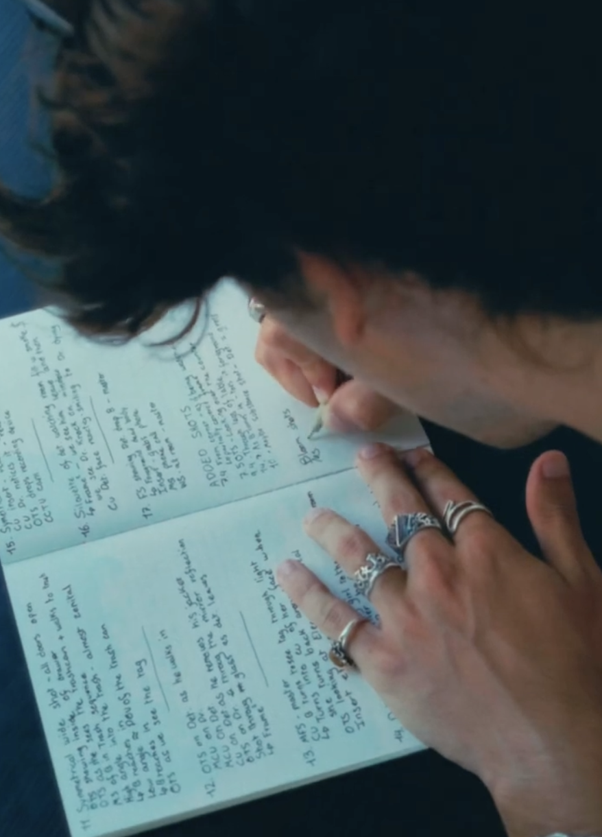 An over-the-shoulder view of a person with rings on their fingers writing in a notebook.