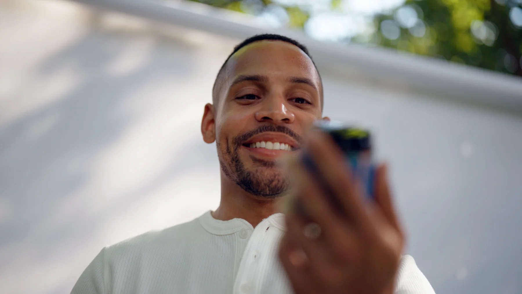 A man in a white shirt smiles while looking down and holding a blurry object.