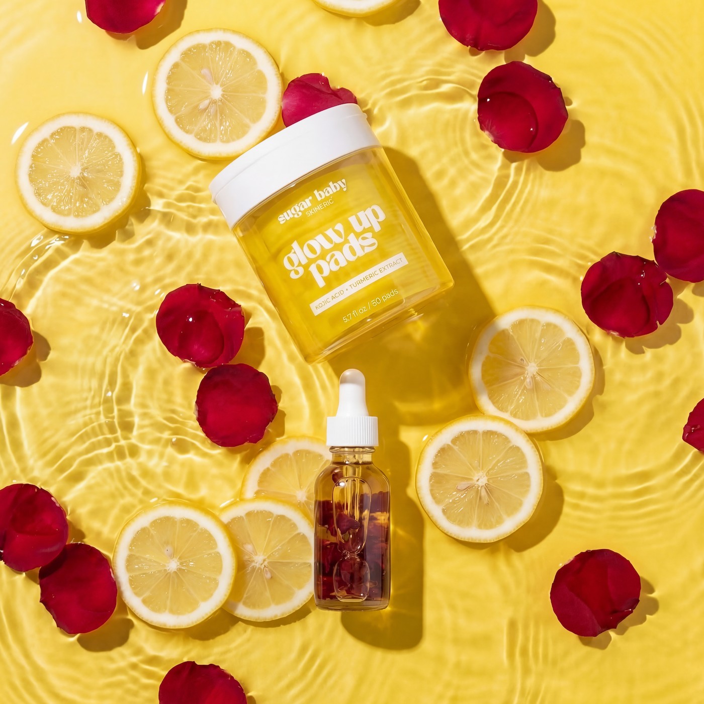 Skincare products, including pads and a serum, float in water with lemon slices and red rose petals.