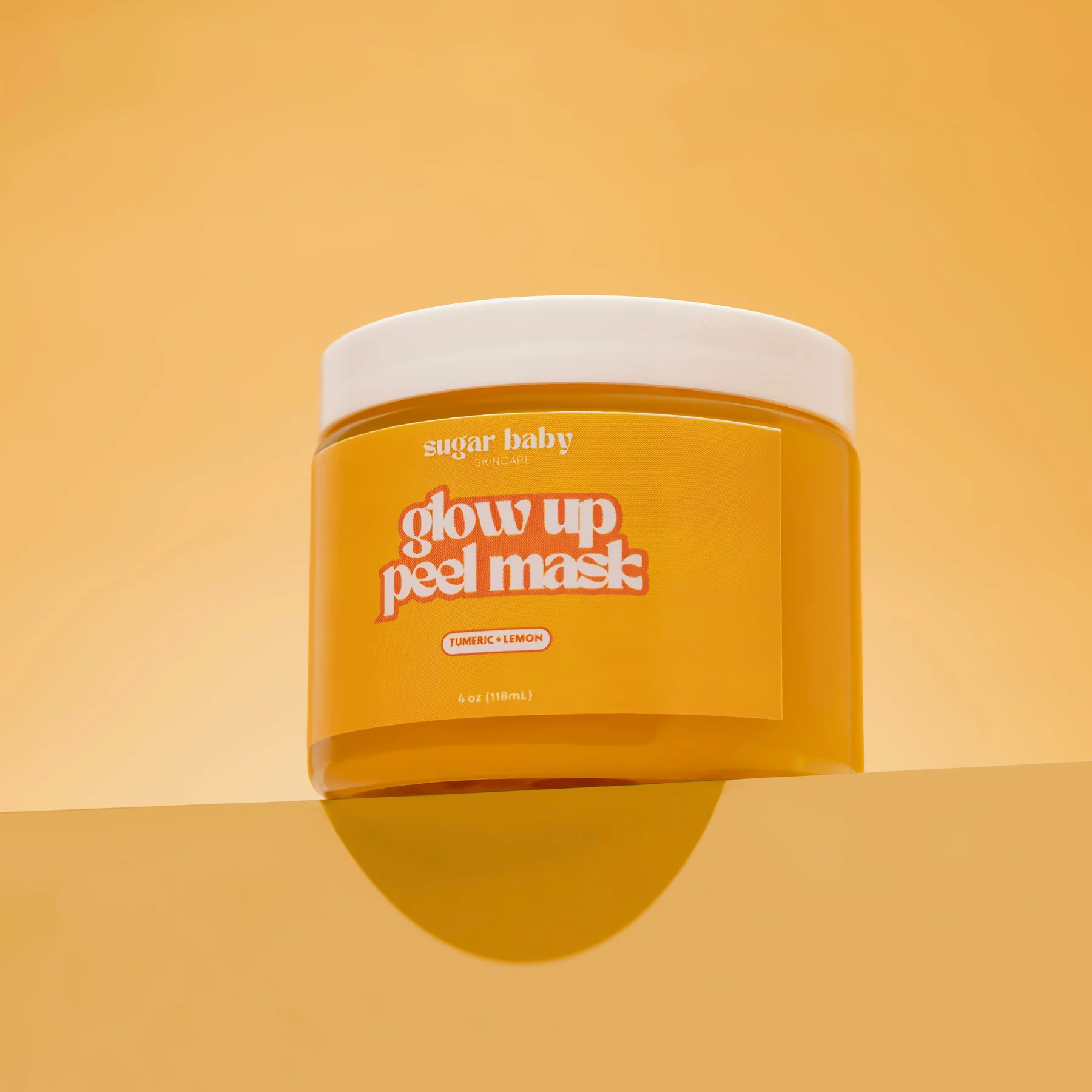 Orange jar labeled 'glow up peel mask' with turmeric and lemon, on a matching background.