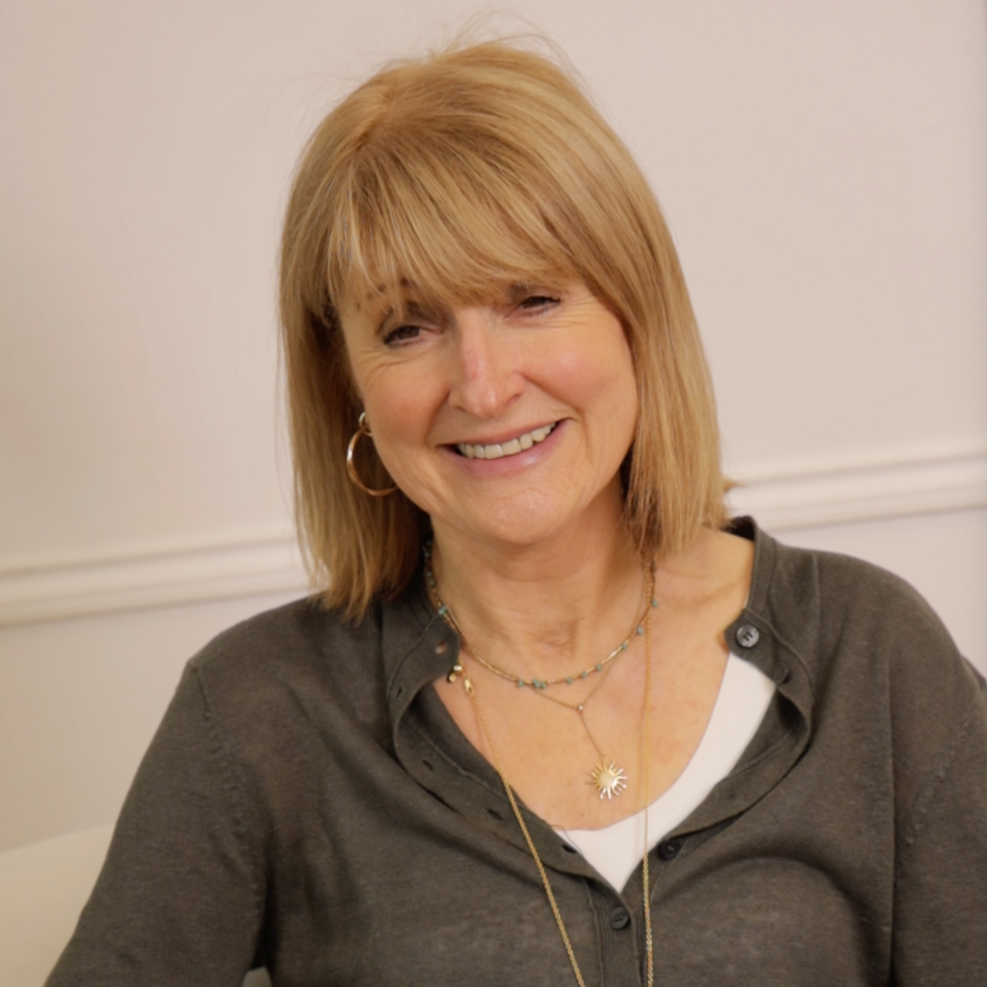 Smiling person with blond hair in a gray shirt against a plain background.
