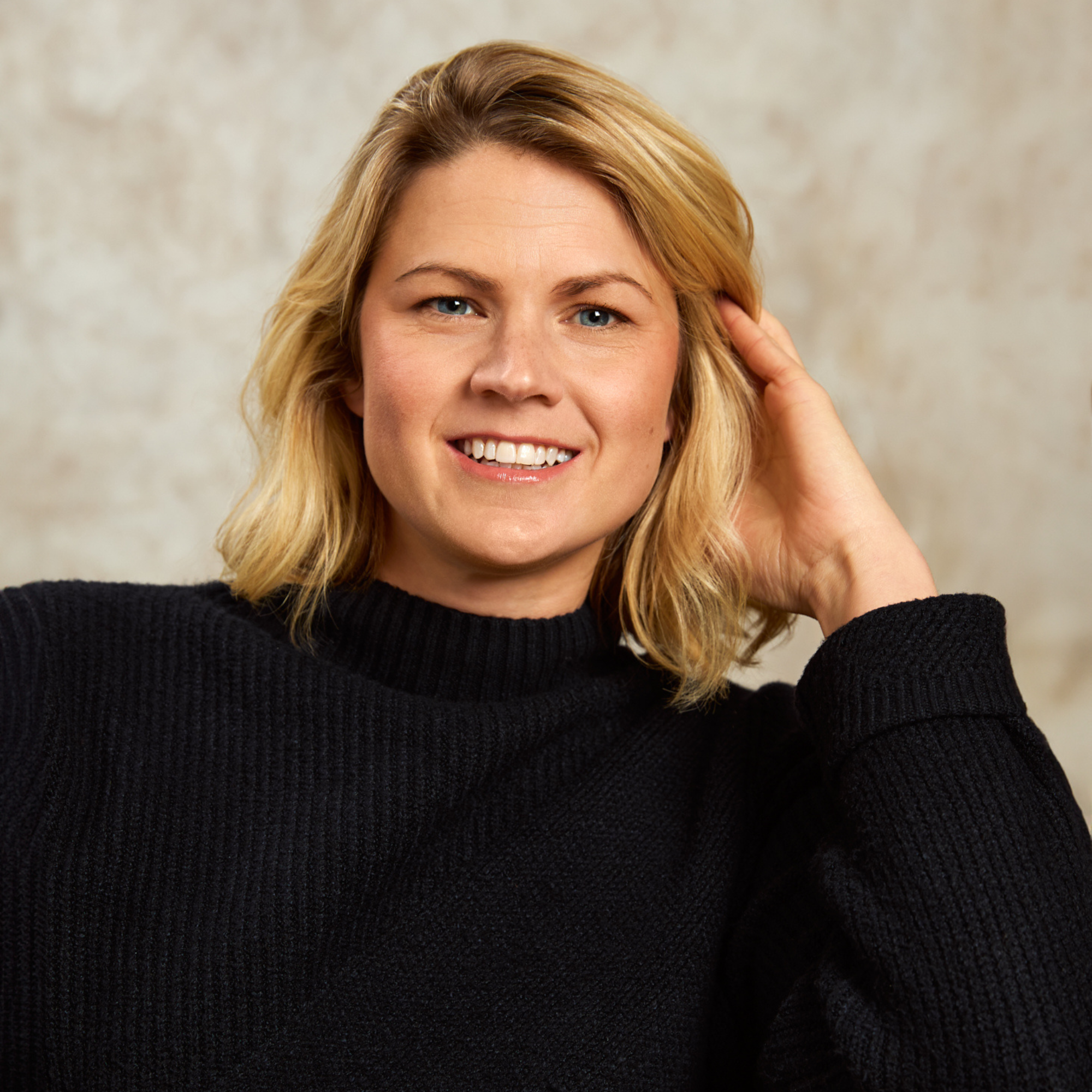 Person smiling, wearing a black sweater, with a neutral background.