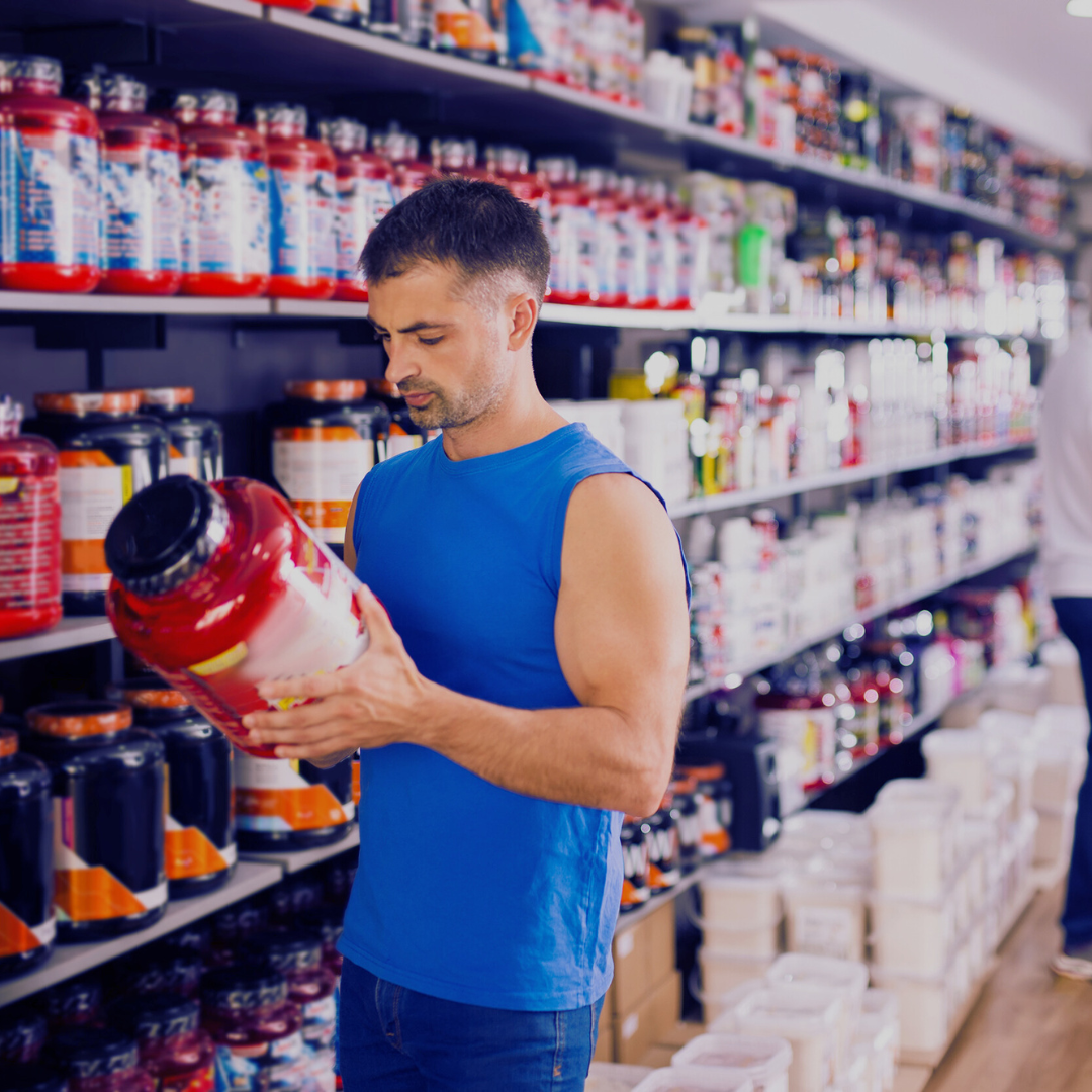 Man in blue shirt examining a large container in a supplement store.