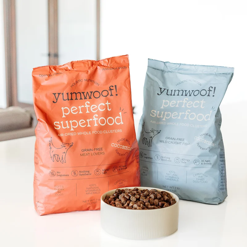 Two bags of Yumwoof dog food with a bowl of brown kibble.