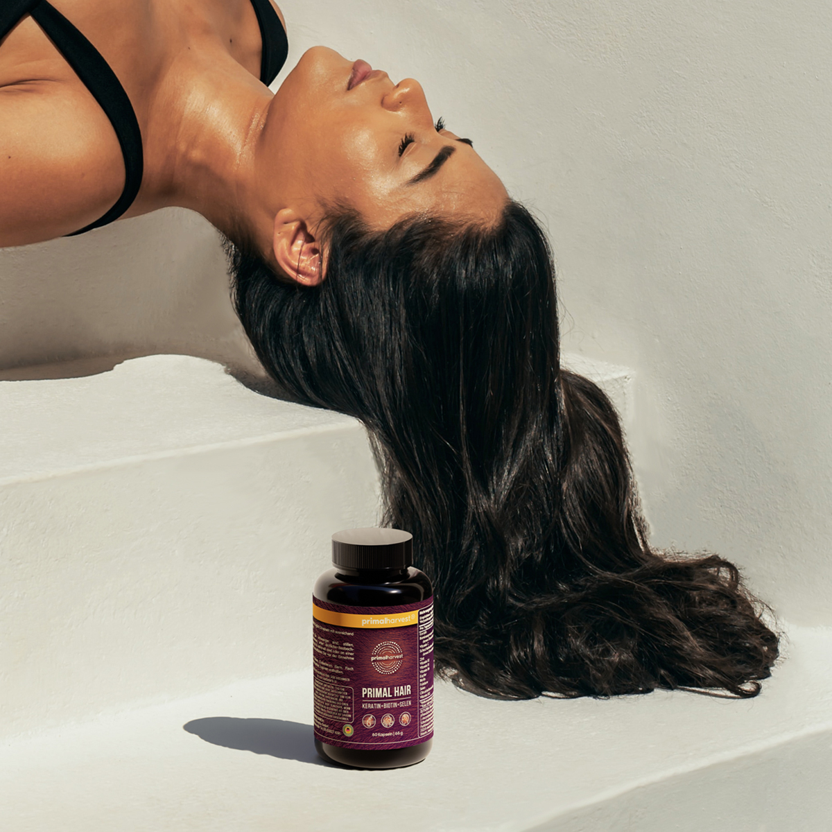 Woman with long hair reclined, next to a bottle of hair supplement.