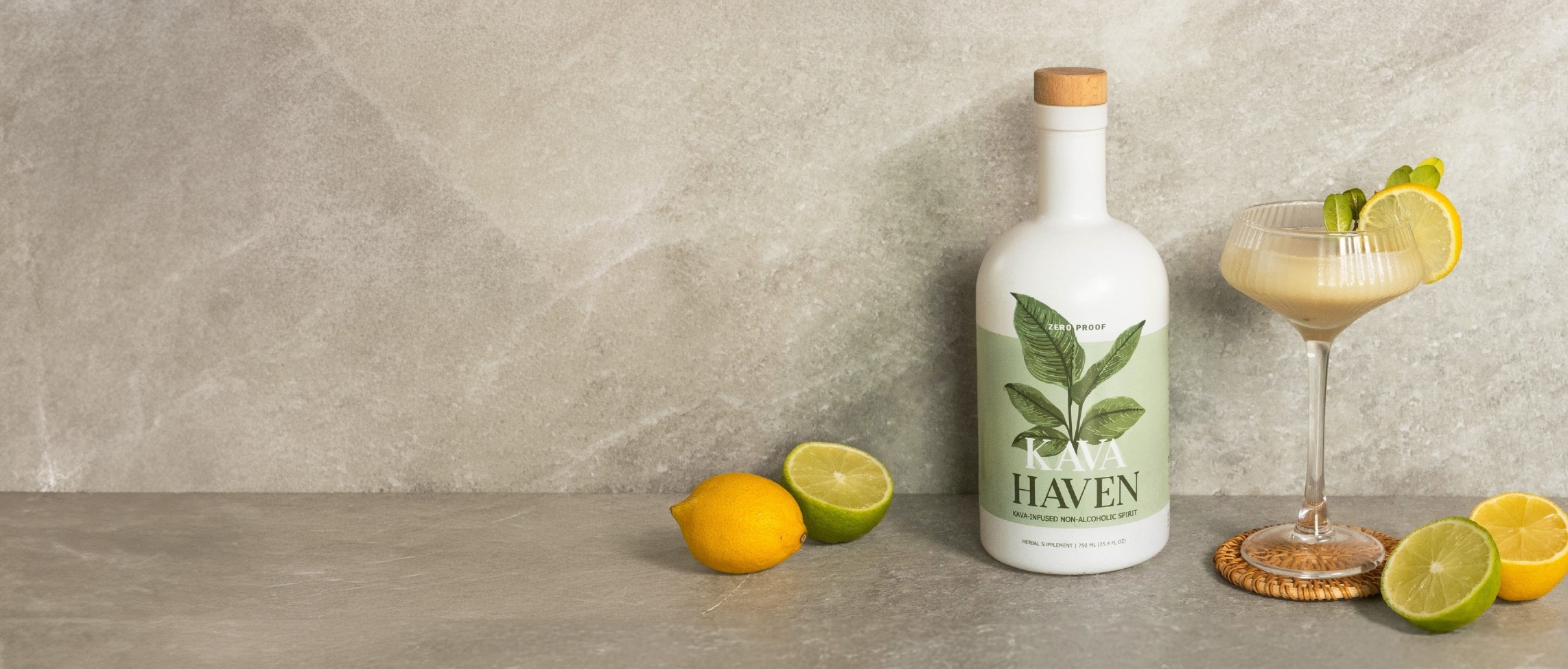 A bottle of Kava Haven non-alcoholic spirit, a gold shaker, a lemon, and two yellow cocktails.