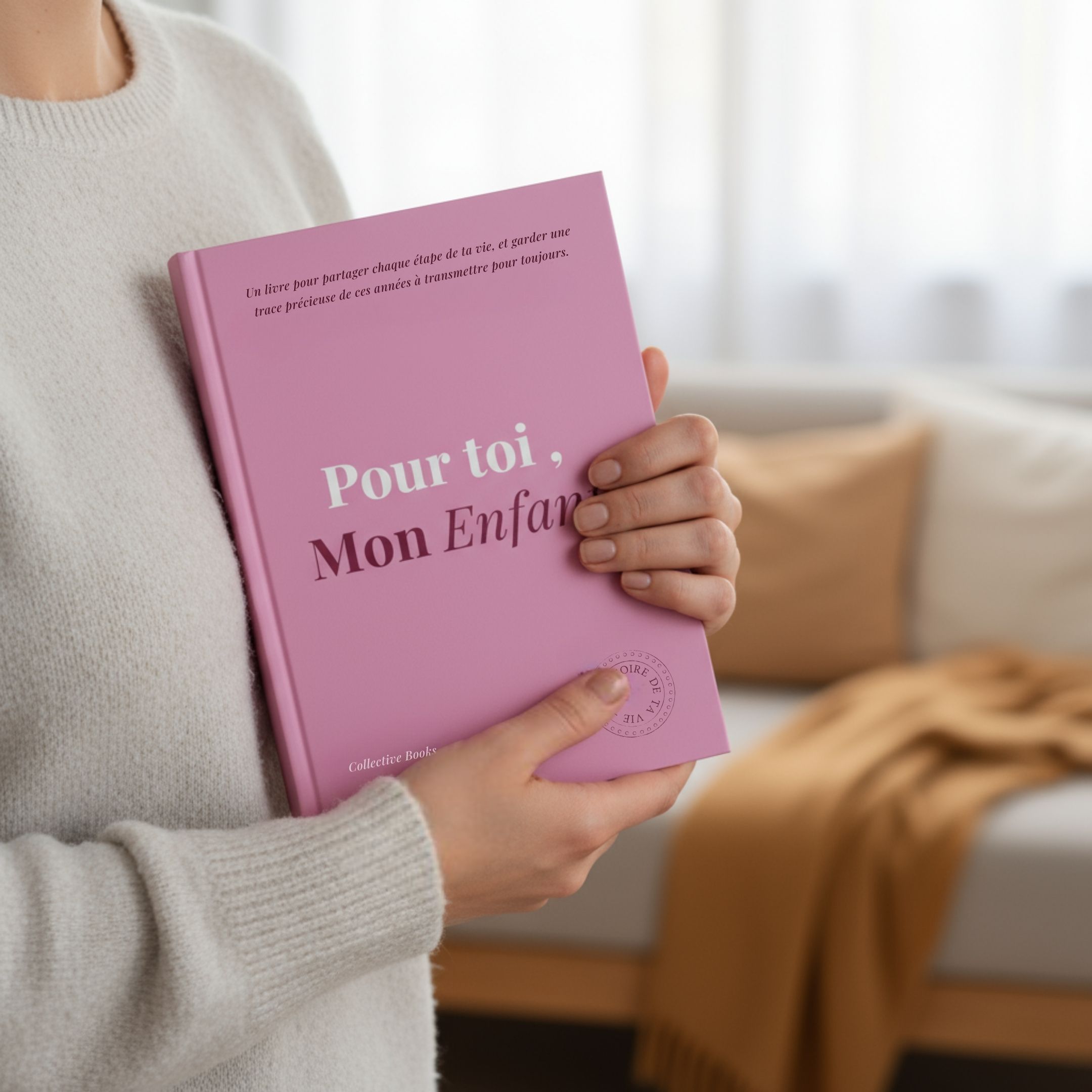 Person holding a pink book titled 'Pour toi, Mon Enfant' with a cozy background.