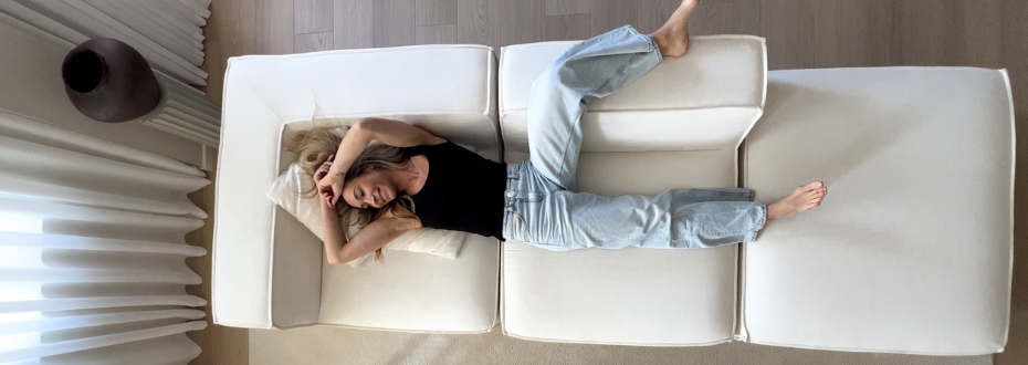 Person lying on a white couch, wearing a black top and jeans.
