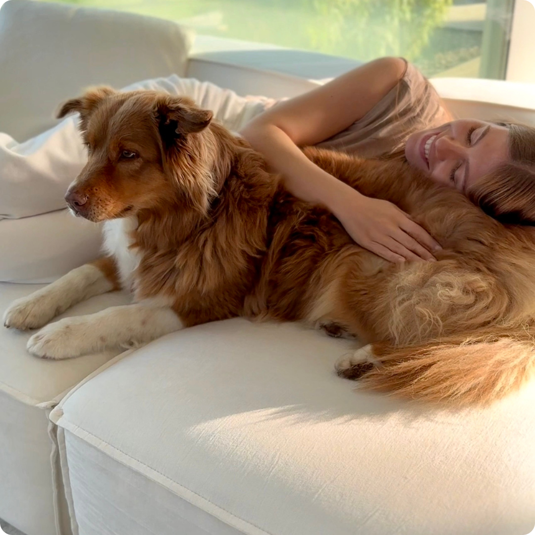 Woman smiling while hugging a brown dog on a white couch.