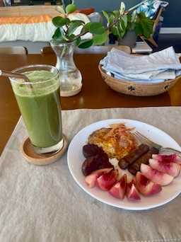 Plate with fruit, sausage, hash browns, and a green smoothie on a table.
