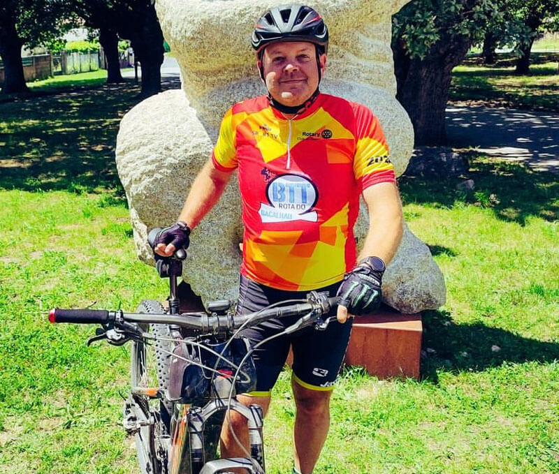 Man in cycling gear standing with a bicycle in a park.