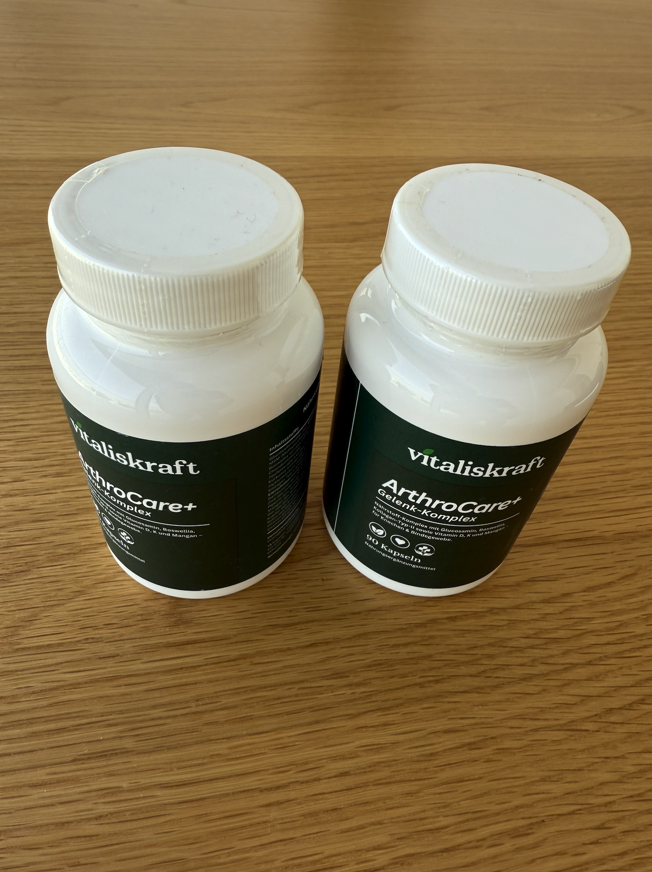 Two white bottles of Vitaliskraft ArthroCare+ supplements sitting on a wooden surface.