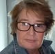 A close-up, slightly blurry photo of a woman with short brown hair and glasses, looking at the camera.
