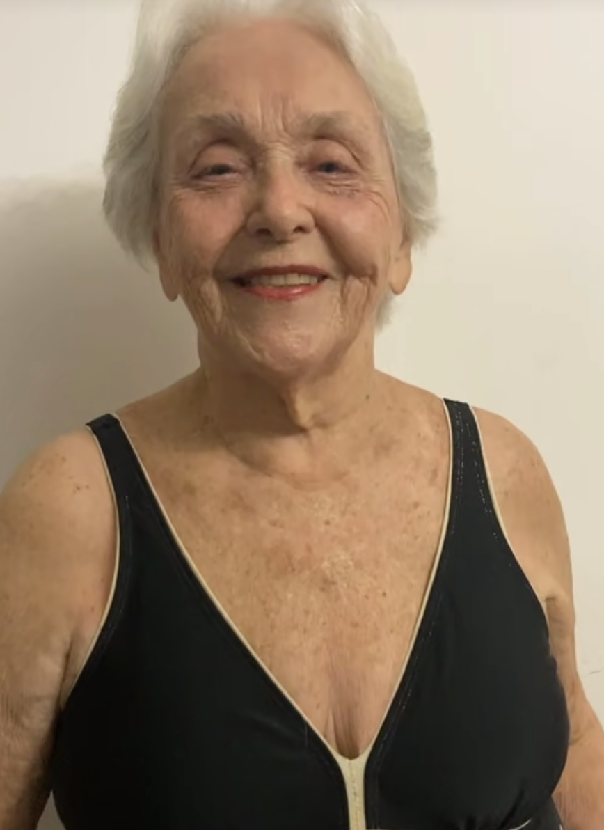 Elderly woman smiling, wearing a black top, against a plain background.