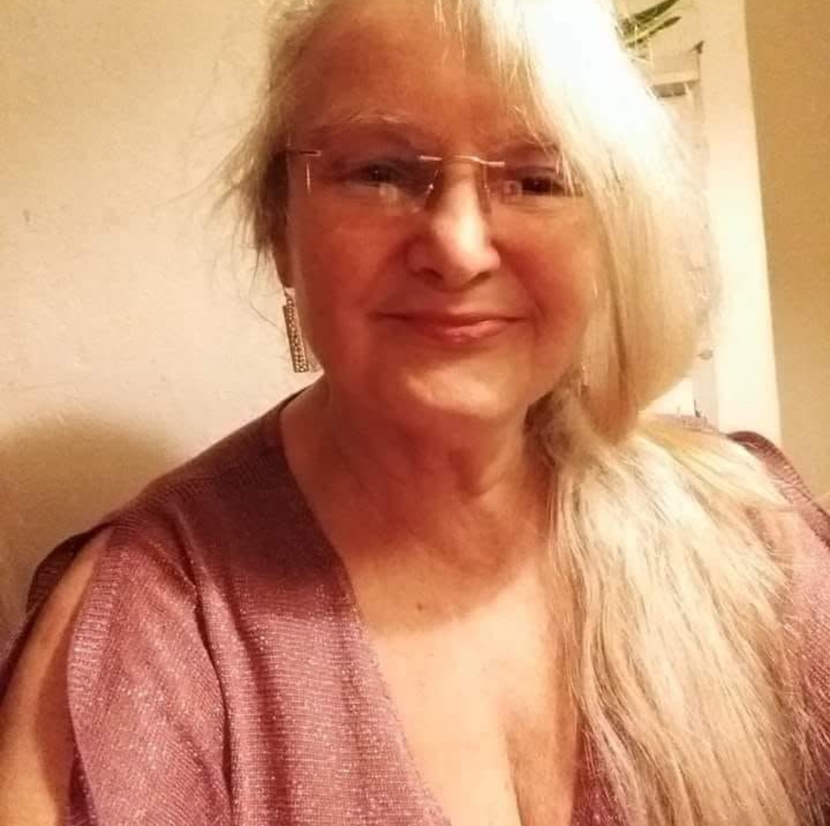 Smiling person with long white hair and glasses, wearing a purple top.