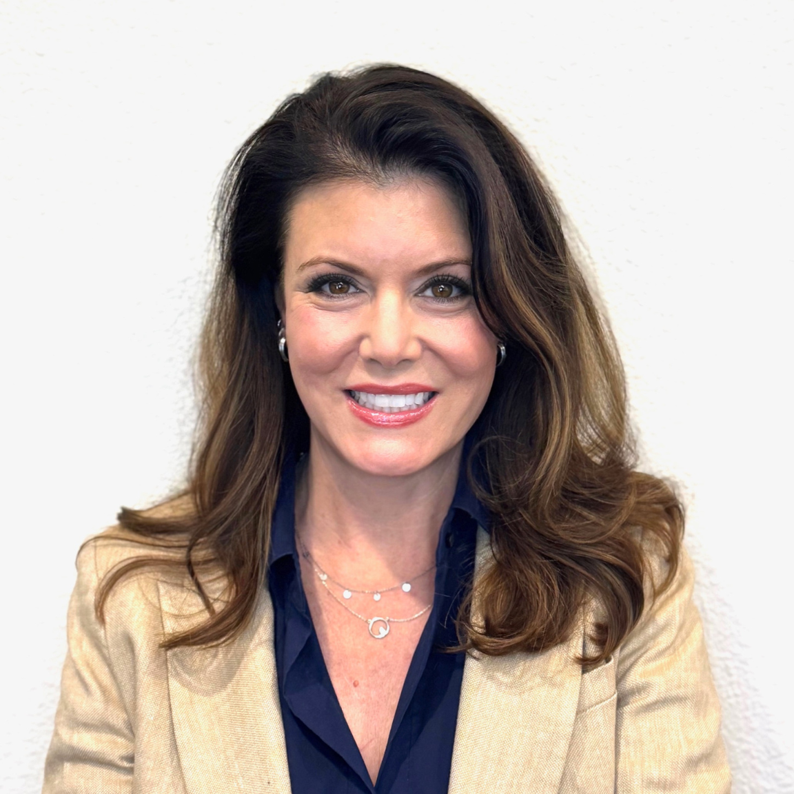 Smiling woman with long brown hair wearing a beige blazer and navy shirt.