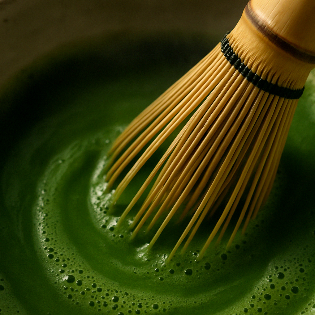 Bamboo whisk stirring frothy green liquid, possibly matcha tea.