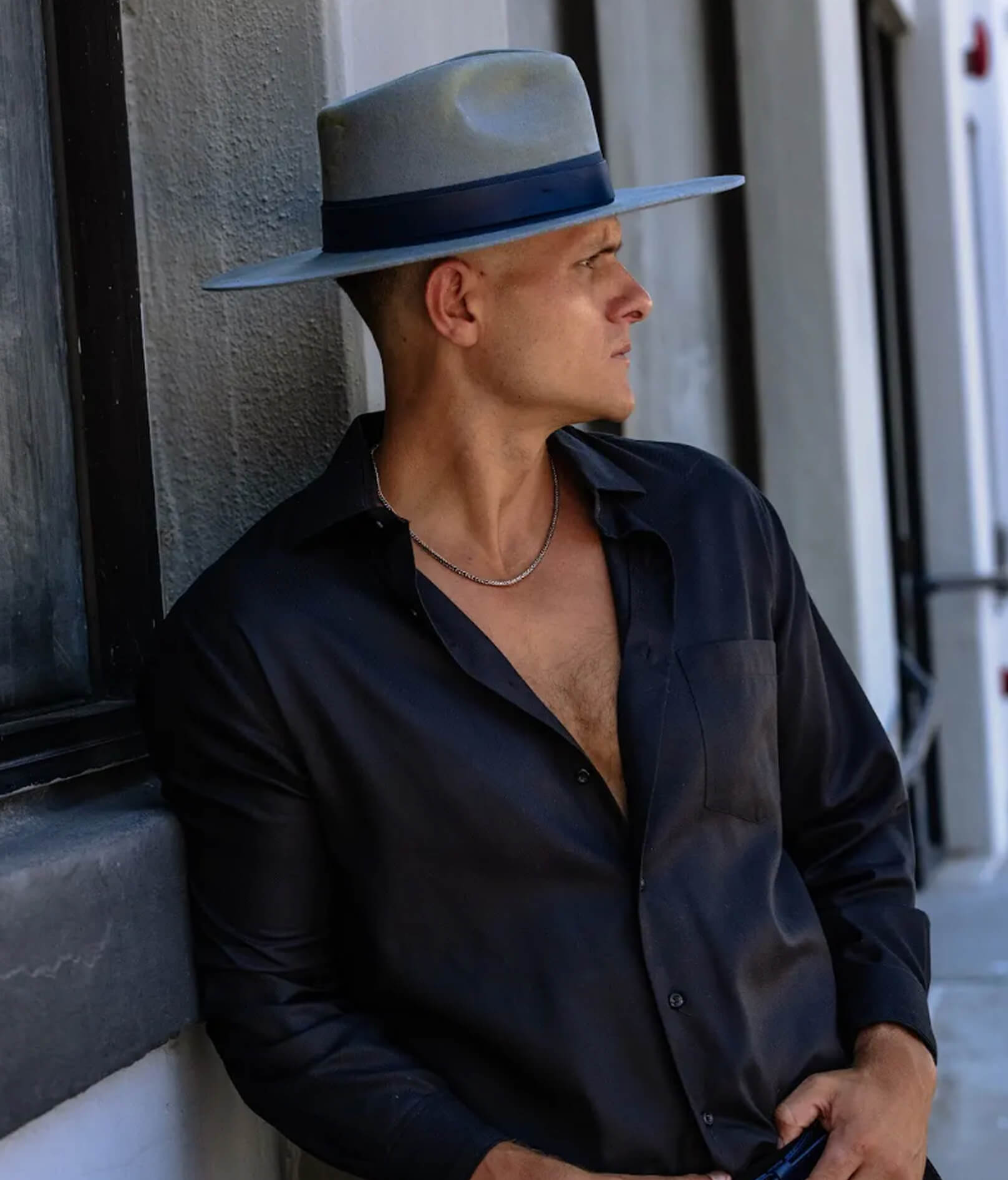 Person in a dark shirt and gray hat looking to the side near a window and wall.