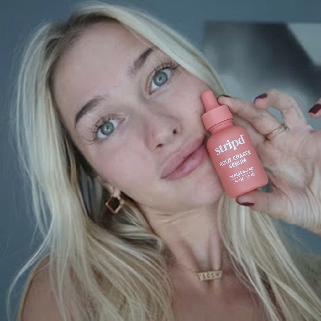 Person holding a bottle of stripd Root Eraser Serum close to face.
