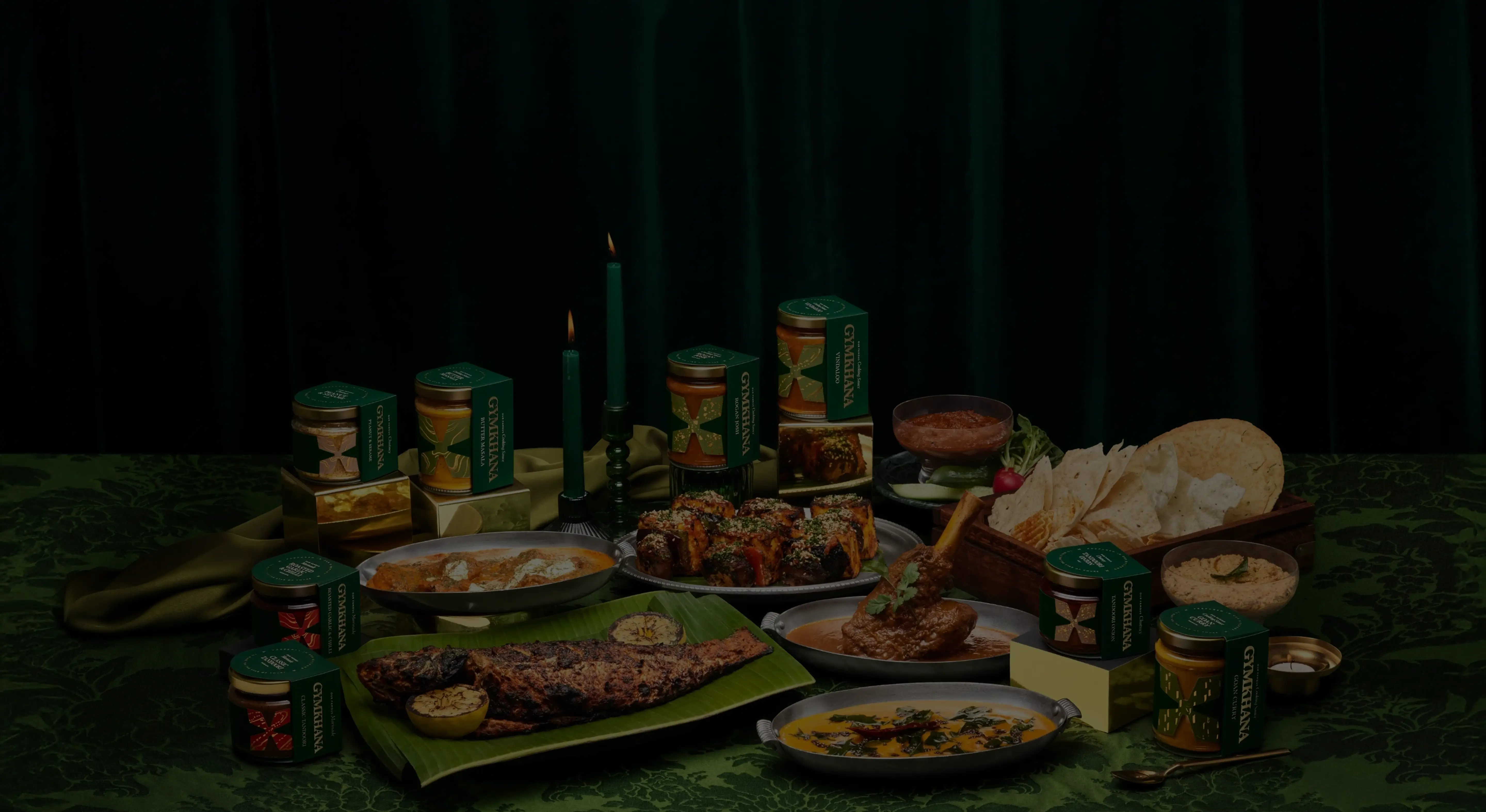 Assorted food dishes and sauces on a green table with candles.
