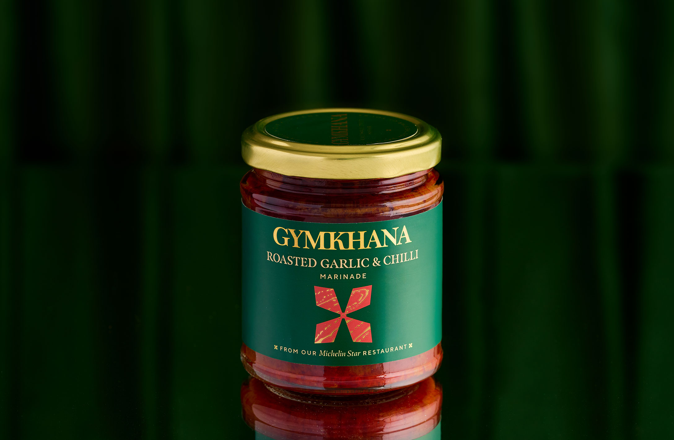 Jar of Gymkhana roasted garlic and chilli marinade on green background.