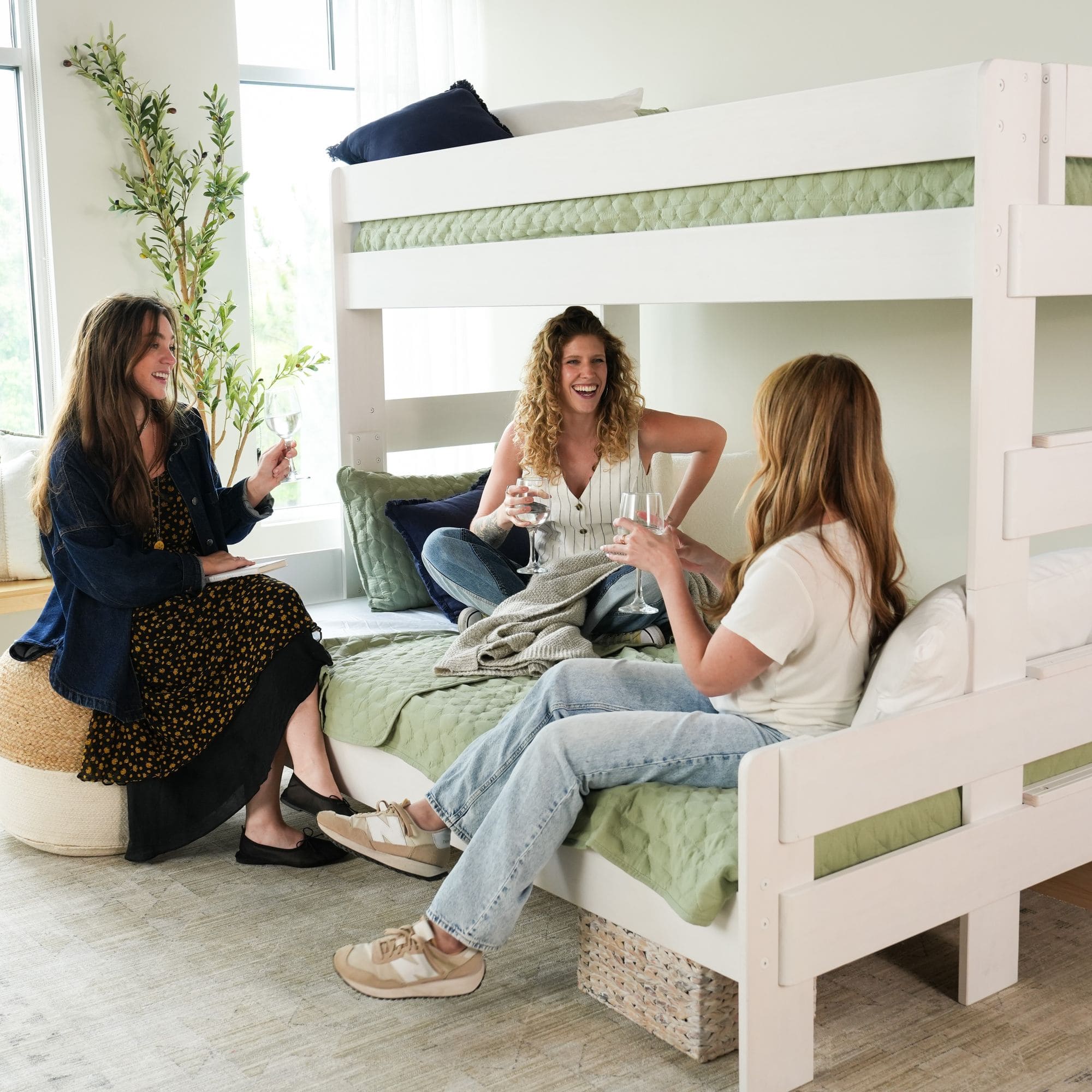 Women enjoying drinks and conversation on a cozy bunk bed in a modern living room setting.