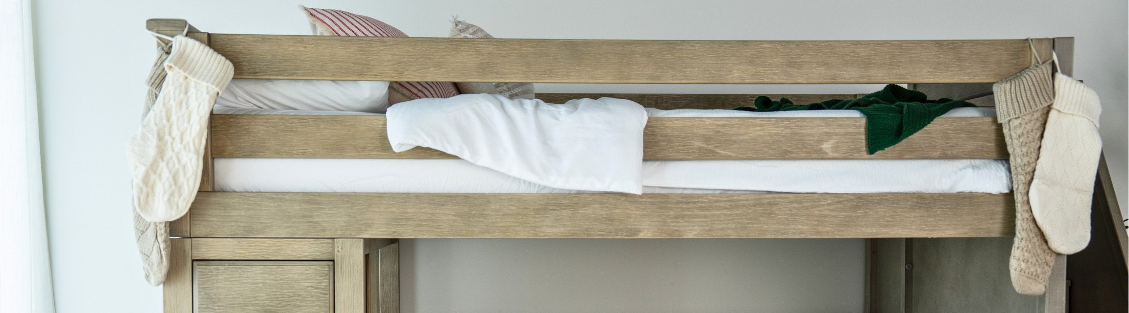 Rustic wooden top bunk bed with white bedding, green throw and knitted Christmas stockings hanging in a neutral farmhouse kids bedroom