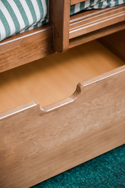 Wooden storage drawer under a bed with a green striped mattress.