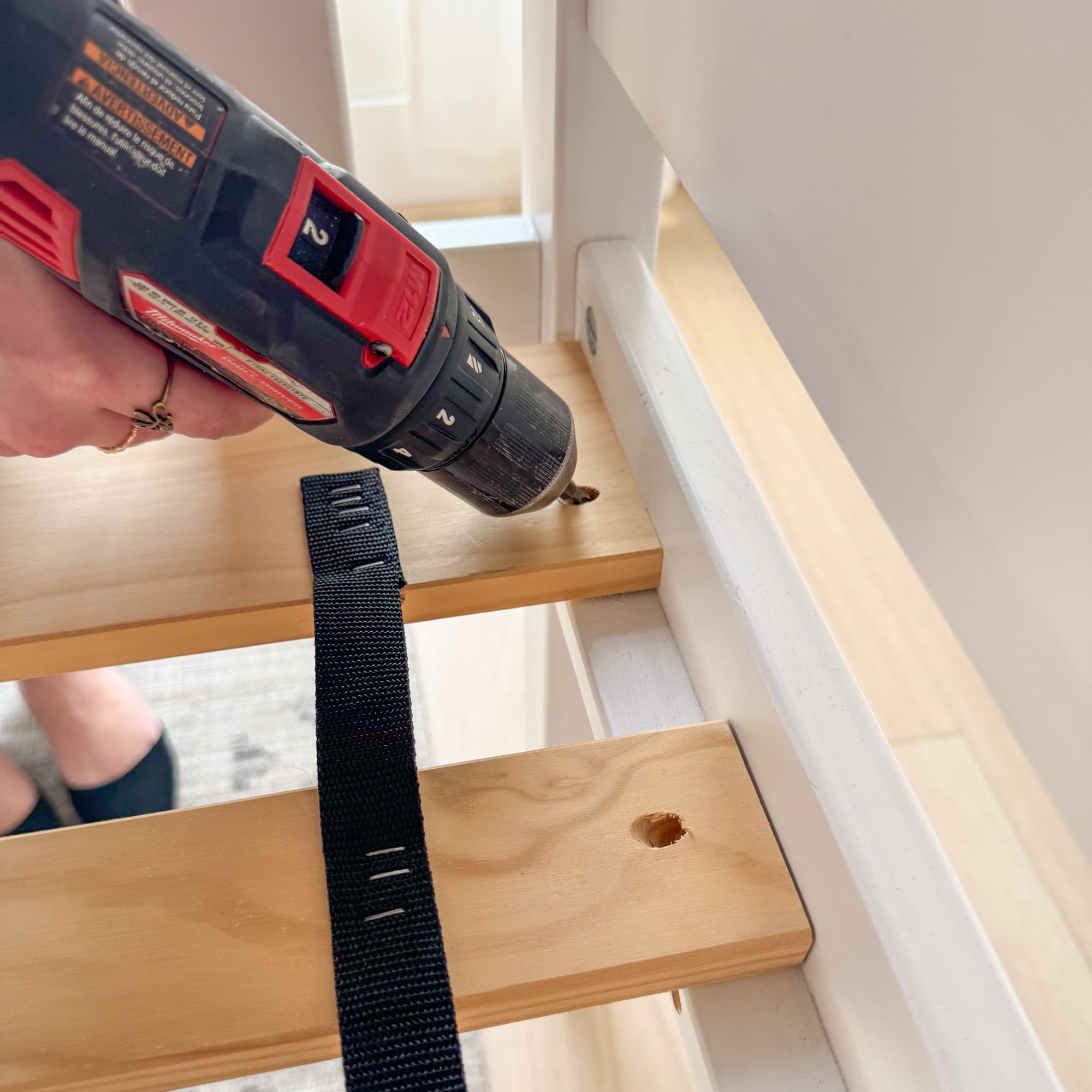 Person using a drill on wooden furniture with a black strap.