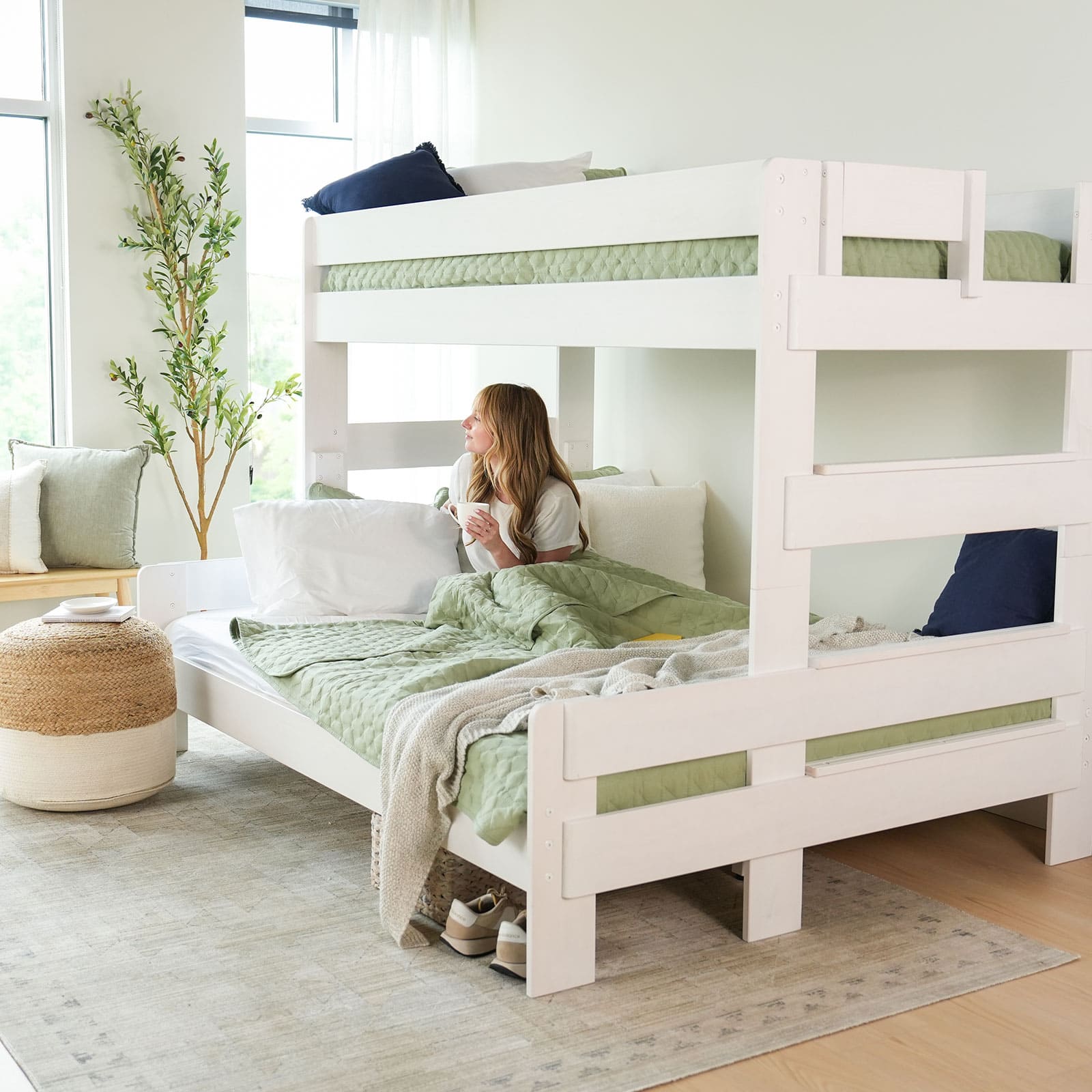 Woman relaxing in a modern bedroom with a white bunk bed and green bedding, creating a cozy and inviting atmosphere.