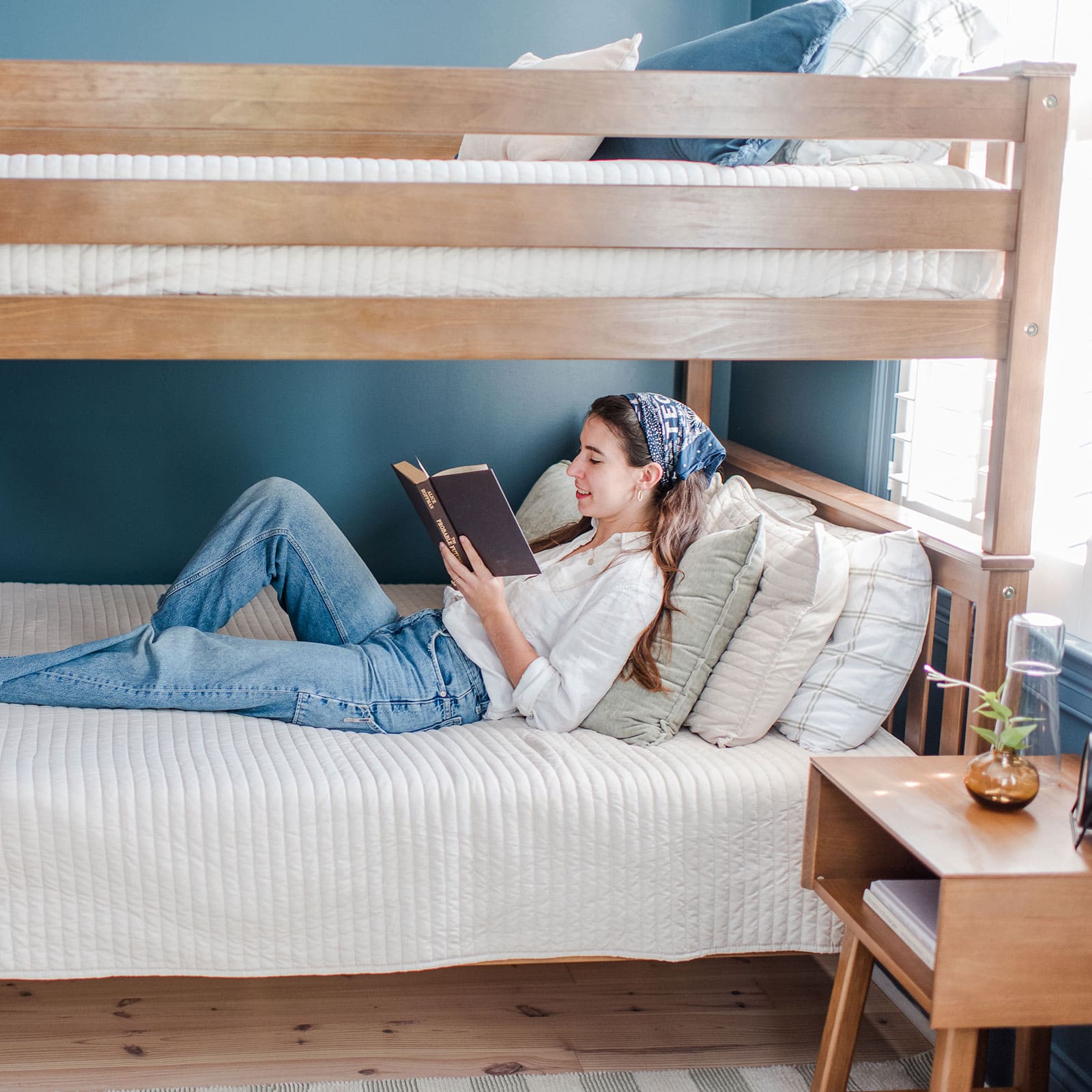 Person reading a book on a lower bunk bed with blue walls.