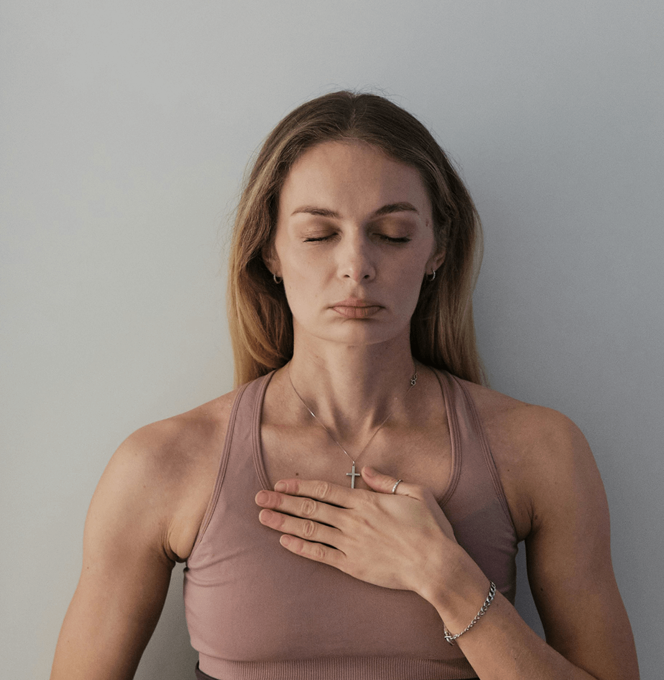 Person meditating with eyes closed and hand on chest, wearing a necklace.