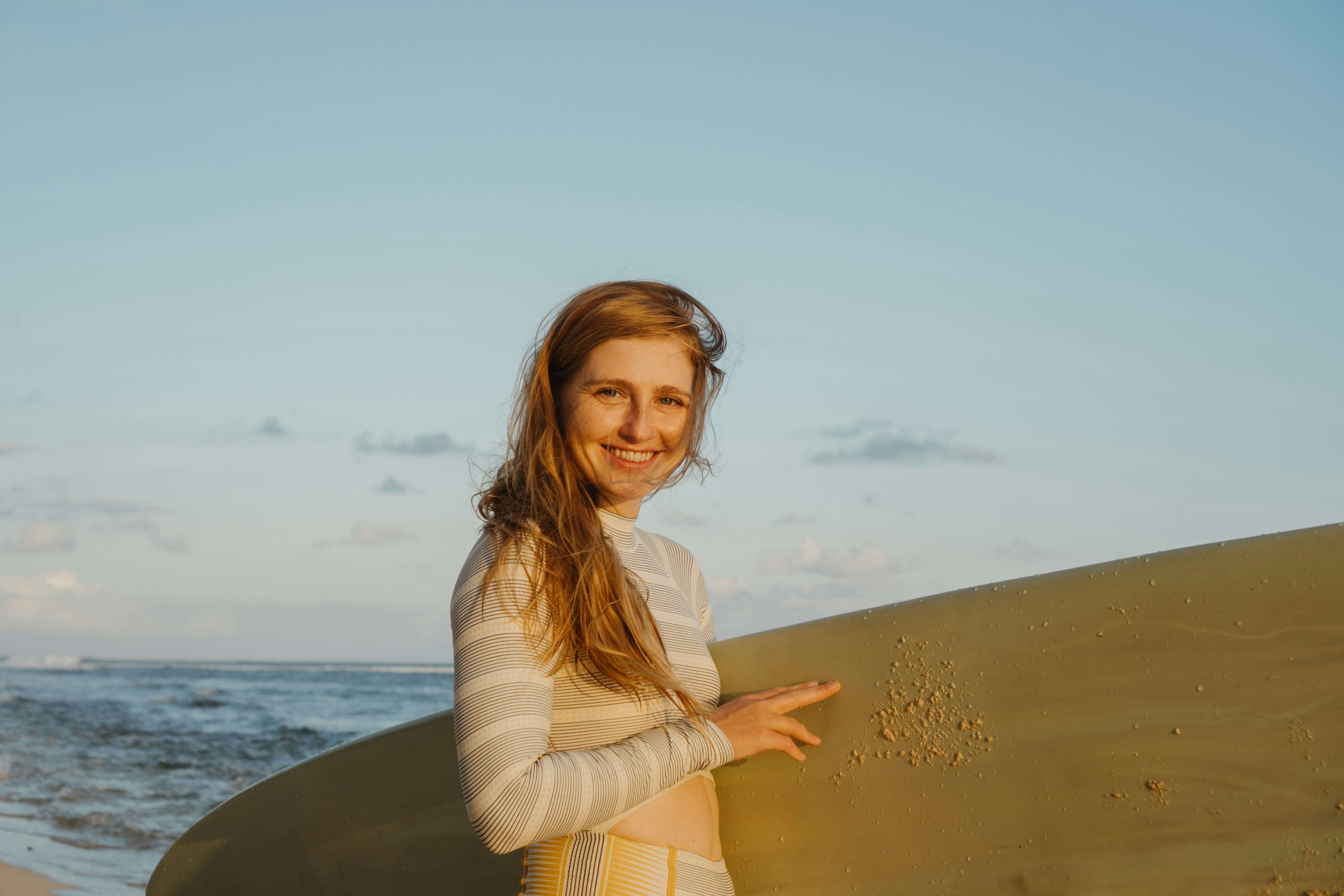 A person smiling while holding a surfboard at the beach.