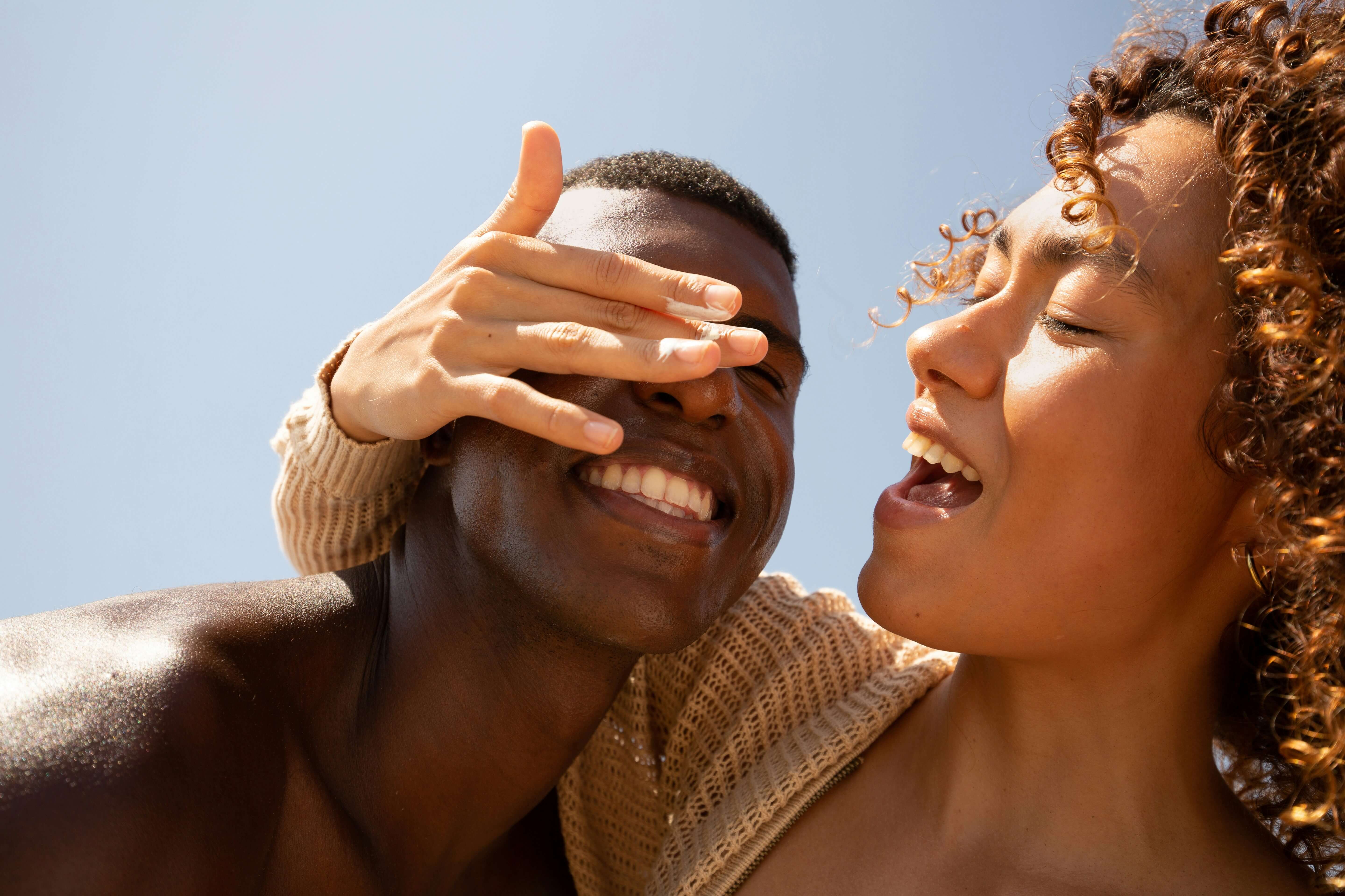 Two people smiling outdoors, enjoying a sunny day together.