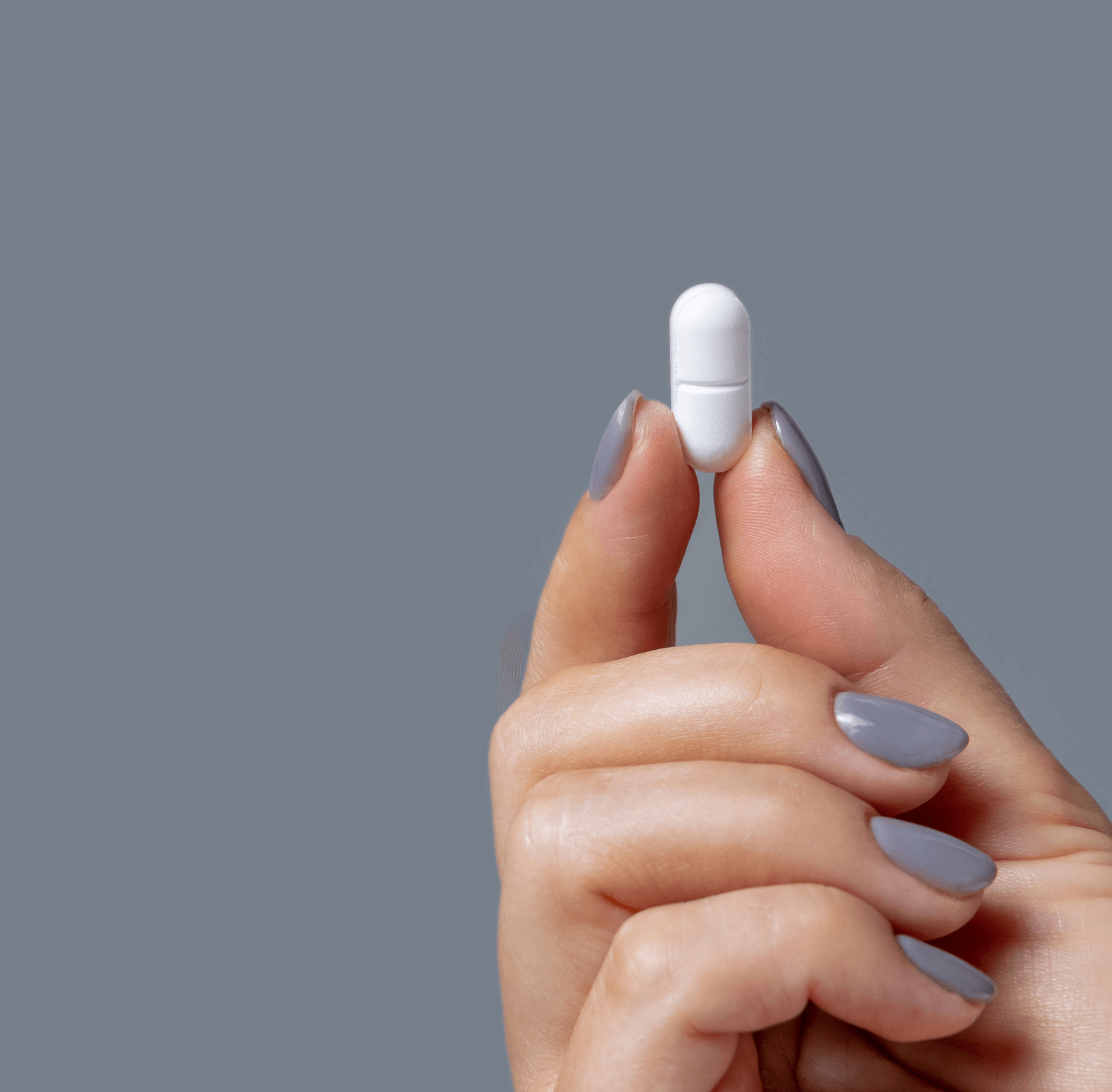 Hand holding a white pill against a gray background.