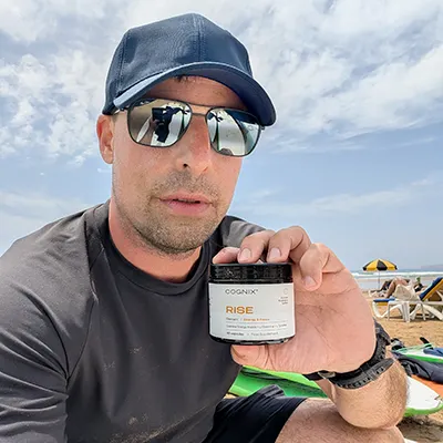 Person in sunglasses holding a jar labeled 'Rise' on a beach.