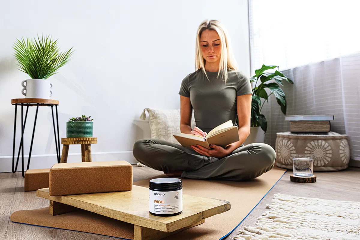 Young woman reading a book on a yoga mat, lifestyle picture. Cognix supplement on yoga block