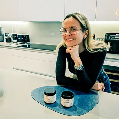 Woman smiling with Cognix and COR supplement bottles in front, photo