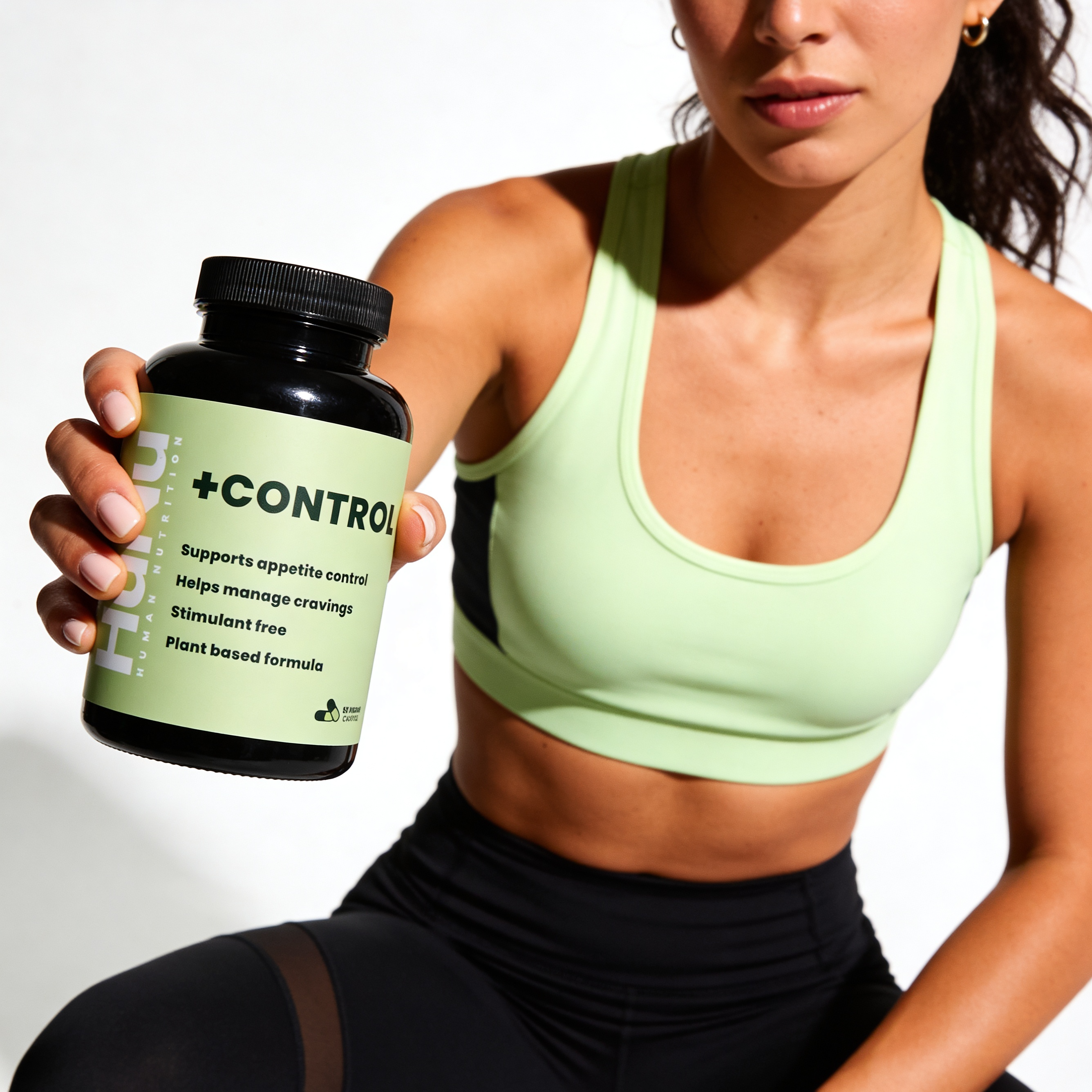 A woman in athletic wear holds up a black bottle of +Control supplements against a white background.