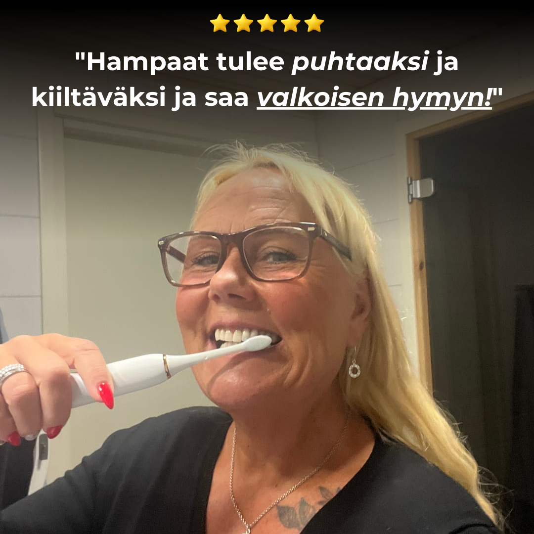 A smiling blonde woman with glasses brushing her teeth with a white electric toothbrush in a bathroom.