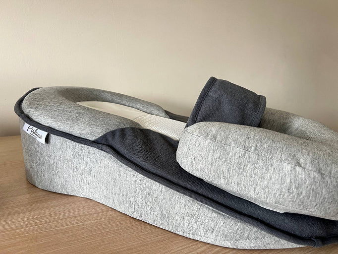 A padded baby lounger in light and dark grey fabric, sitting on a wooden surface.