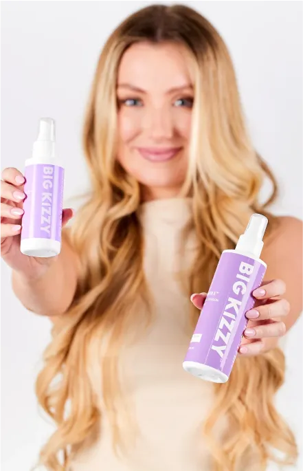 Person holding two Big Kizzy hair product bottles.