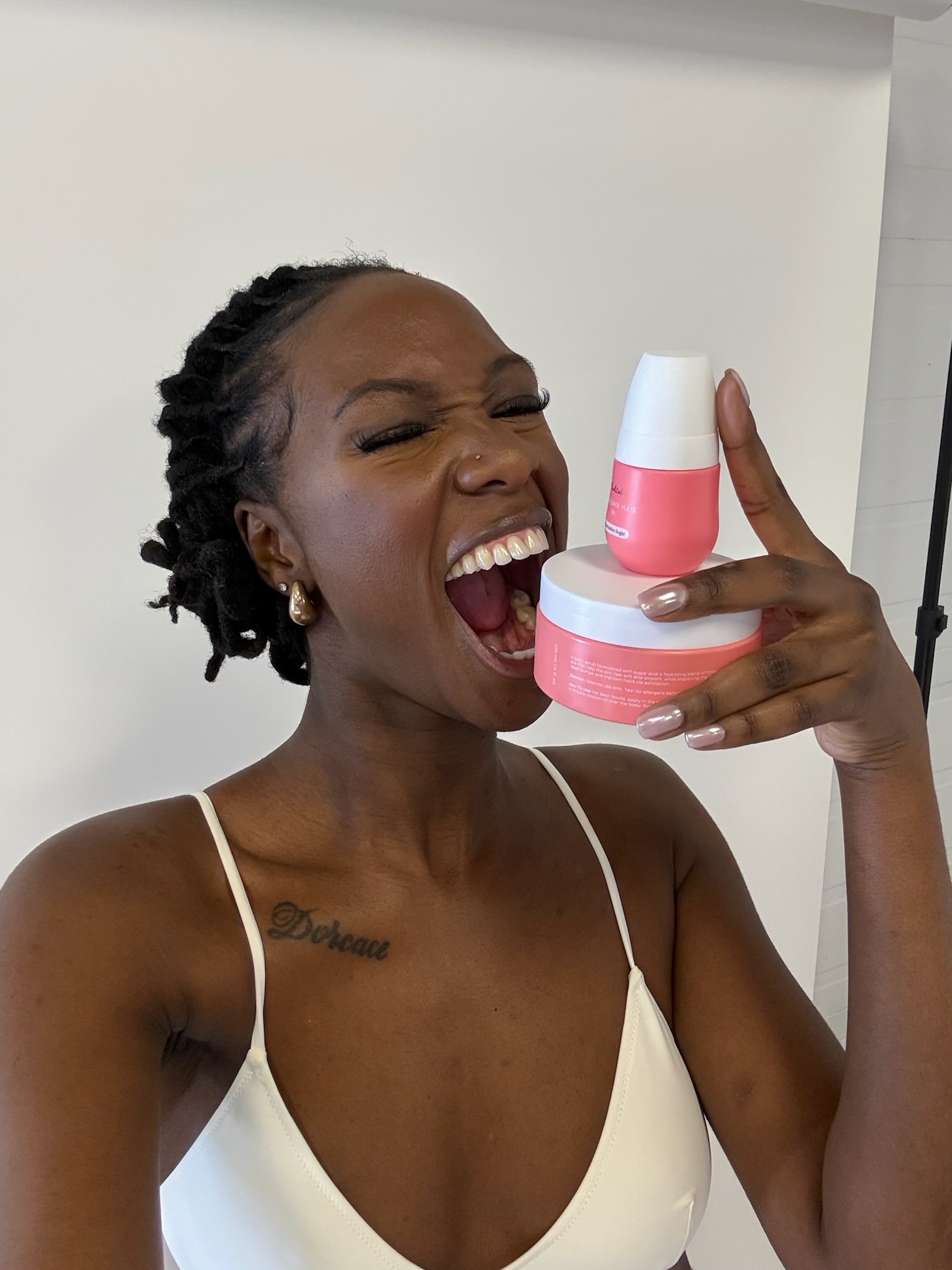 Person playfully holding pink skincare products, smiling with eyes closed.