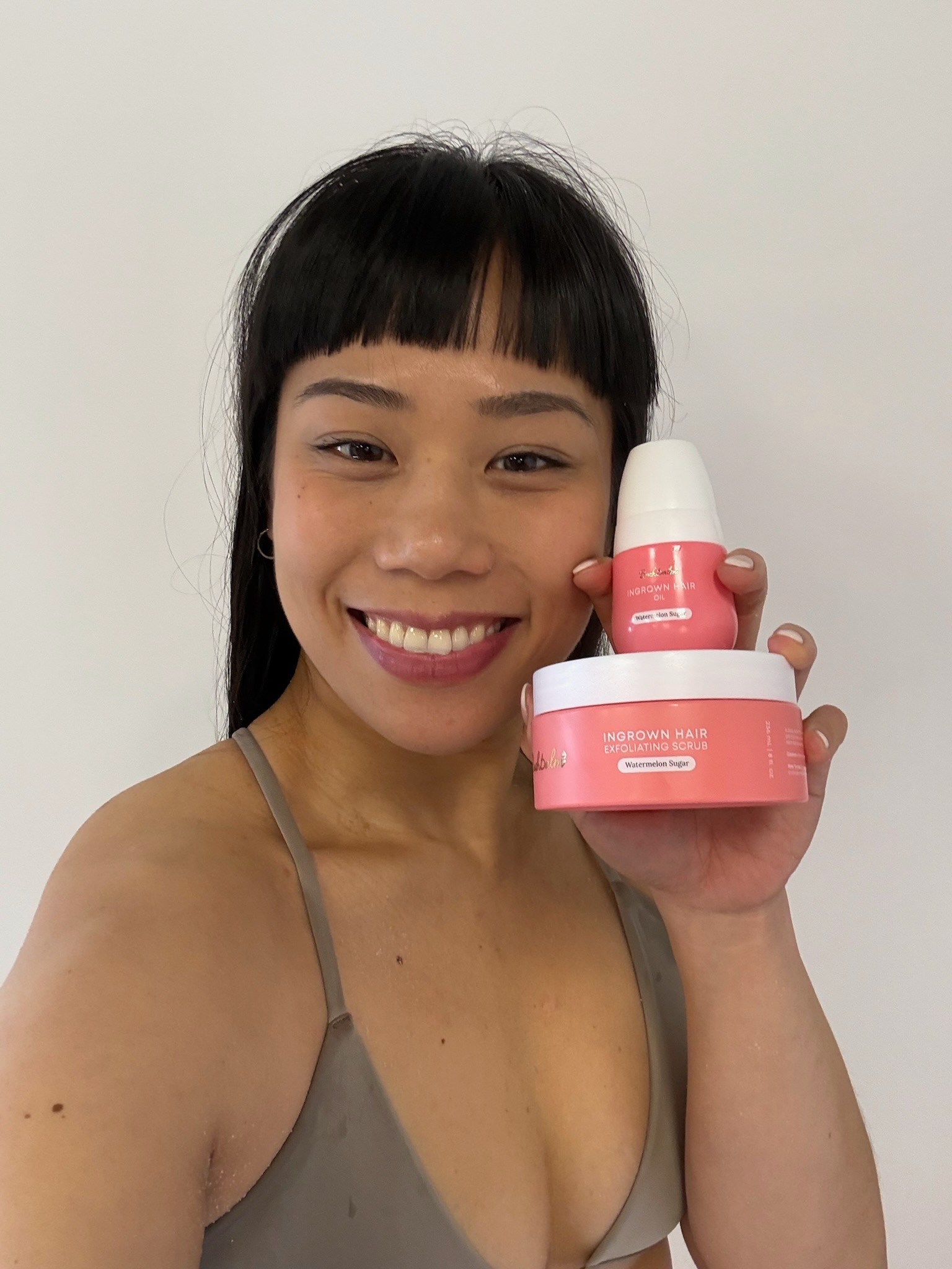 Person smiling, holding ingrown hair products against a plain background.