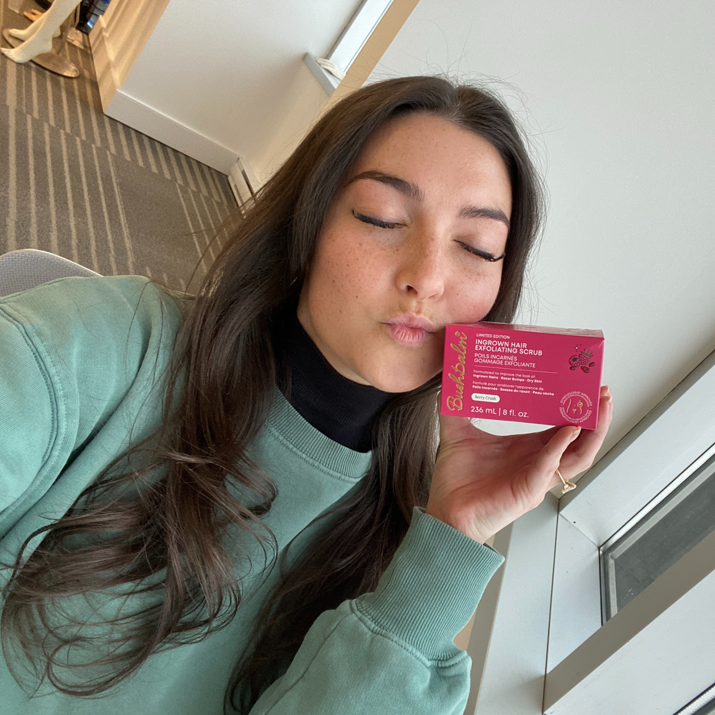 Person holding a pink box of exfoliating scrub, with eyes closed.