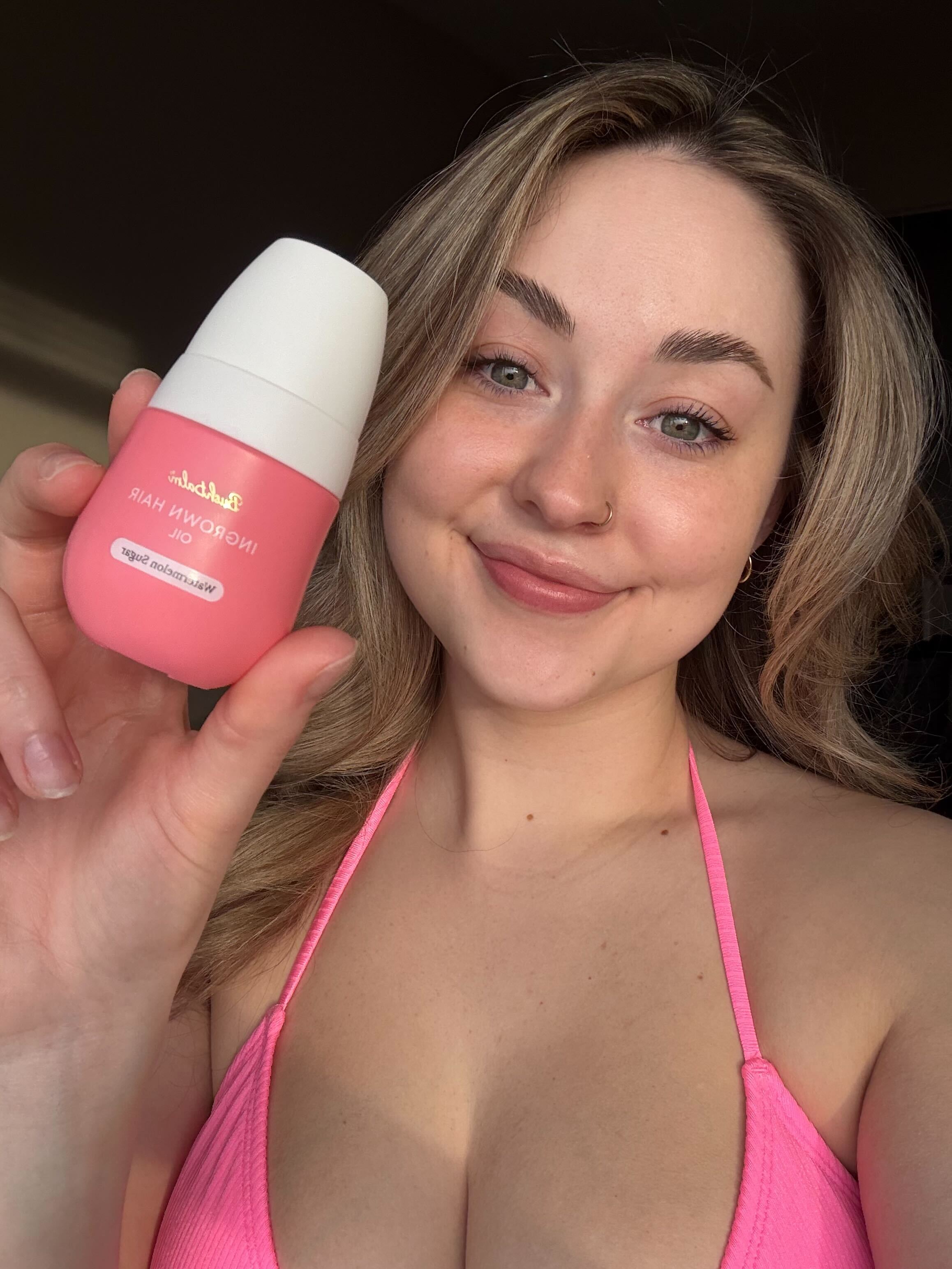 Person holding a pink bottle labeled 'Hair Growth Oil' and smiling.